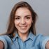 Smiling Woman in shirt making selfie in studio and looking at camera. Isolated gray background